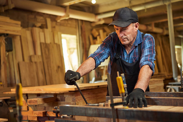 Portrait d'un menuisier chevronné en uniforme collant des barres de bois avec des pressions à la main à la menuiserie - Photo, image