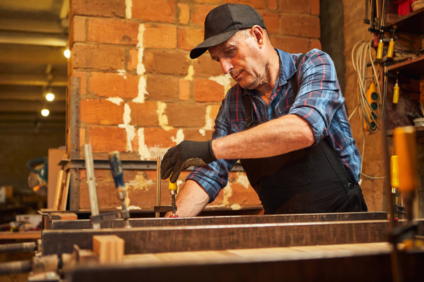 Retrato de un carpintero mayor en barras de madera de encolado uniforme con presiones de mano en la fabricación de carpintería - Foto, imagen