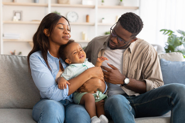 Parents afro-américains assis avec un enfant en pleurs sur le canapé - Photo, image