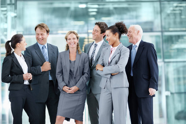 Unterstützt von ihrem stolzen Team von Mitarbeitern. Positive Gruppe von Geschäftsleuten, die zusammen stehen und lächeln, während sie einen Mitarbeiter umgeben - Porträt. - Foto, Bild