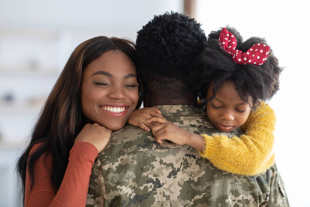 Счастливого воссоединения. Радостная жена и дочь обнимают военного, крупный план - Фото, изображение
