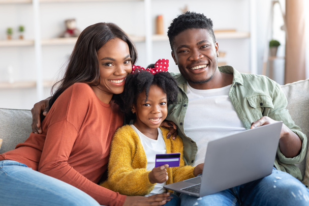 Onnellinen musta perhe kannettavalla tietokoneella ja luottokortilla rentoutuen kotona - Valokuva, kuva