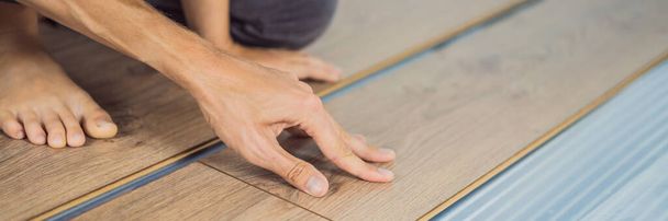 BANNER, LONG FORMAT Father and son installing new wooden laminate flooring on a warm film floor. Infrared floor heating system under laminate floor - Foto, Imagem