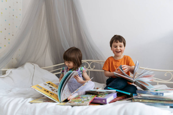 Δύο αδέλφια διαβάζουν βιβλία στον καναπέ, ενώ ο ένας γελάει. - Φωτογραφία, εικόνα