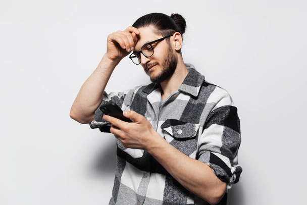 Portrét atraktivního mladíka v kostkované košili s chytrým telefonem v ruce. - Fotografie, Obrázek