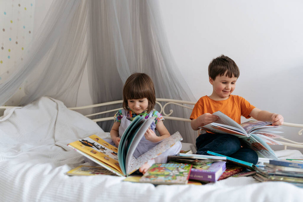 İki kardeş kanepede kitap okurken, bir tanesi gülüyor. - Fotoğraf, Görsel