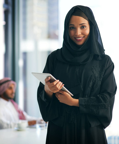So many great apps to keep business running smoothly. Portrait of a young muslim businesswoman holding a digital tablet with her colleague working in the background. - Foto, Bild