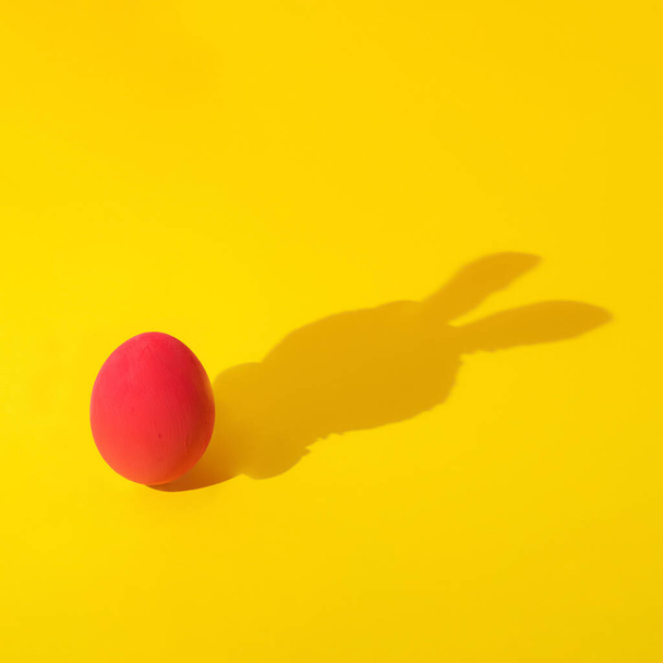 creative concept of red easter egg with rabbit shadow on yellow background . minimal composition. - Foto, immagini