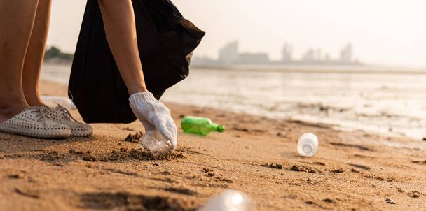 Volunteer woman picking plastic bottle into trash plastic bag black for cleaning the beach, female clean up garbage, Ecology concept and World Environment Day, Save earth concept - Foto, afbeelding