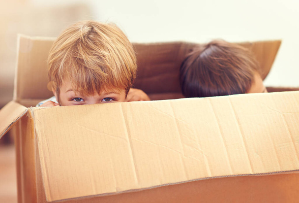 Wanna play a game of peek a boo. Two adorable young boys peeking out of a cardboard box. - Photo, Image