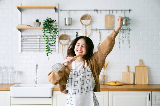 Asiatische junge Frau tanzt in der Küche. Sie glücklich und entspannt in der Freizeit am Wochenende - Foto, Bild