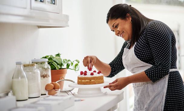 私はベーキング以上のものが大好きです。彼女の台所でケーキを飾る女性の作物のショット. - 写真・画像