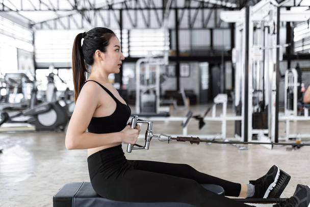 Концепция упражнений Женщина в спортивном топе, обтягивающих штанах и черных кроссовках сидит и концентрируется на вытягивании гибкой веревки из сиденья. - Фото, изображение