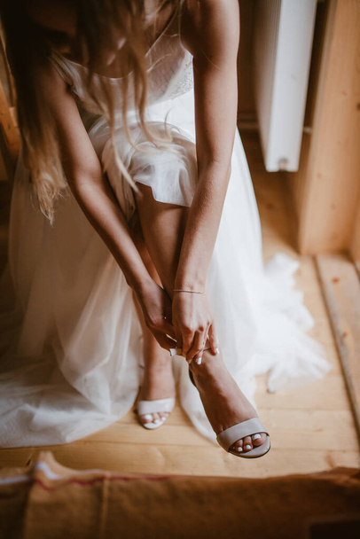 Крупный план портрета невесты руки надевают элегантные бежевые туфли сидя на стуле идол. Свадебная подготовка. - Фото, изображение