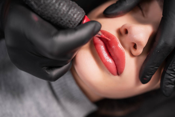 Primer plano de los labios femeninos hinchados durante la aplicación de maquillaje permanente. Tatuaje en la cara y micropigmentación de los labios. Micrófono facial profesional. Aparatos cosmetológicos femeninos. - Foto, Imagen