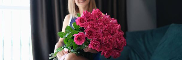 Jonge mooie glimlachende vrouw zit met een groot boeket rozen - Foto, afbeelding