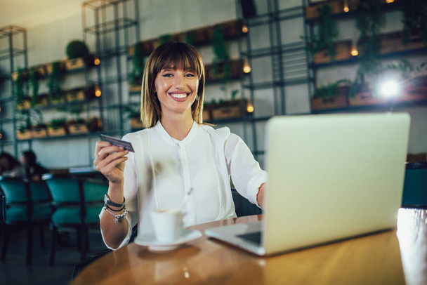 Junge Frau sitzt in Cafeteria und nutzt Kreditkarte für Online-Einkäufe - Foto, Bild