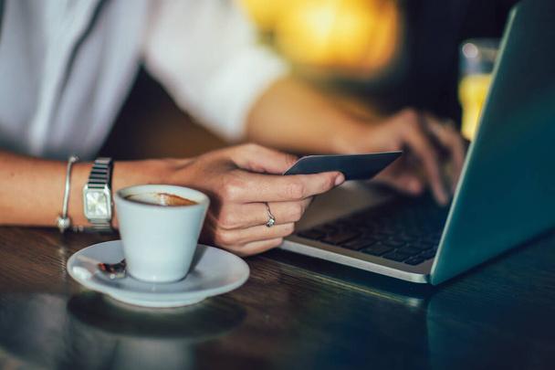 Mujer joven sentada en la cafetería y utilizando la tarjeta de crédito y el ordenador portátil, de cerca - Foto, Imagen