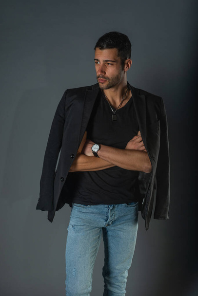 Handsome fashionable model in a black t-shirt with a jacket on his shoulders posing in a studio - Фото, зображення