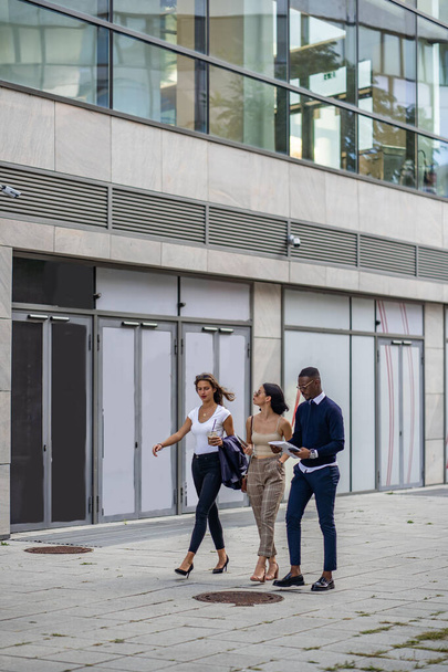 Τρεις πολυφυλετικοί όμορφοι επιχειρηματίες περπατούν ενώ μιλάνε μεταξύ τους. - Φωτογραφία, εικόνα