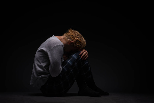 грустный и подавленный мальчик сидит на земле и плачет в одиночестве. - Фото, изображение