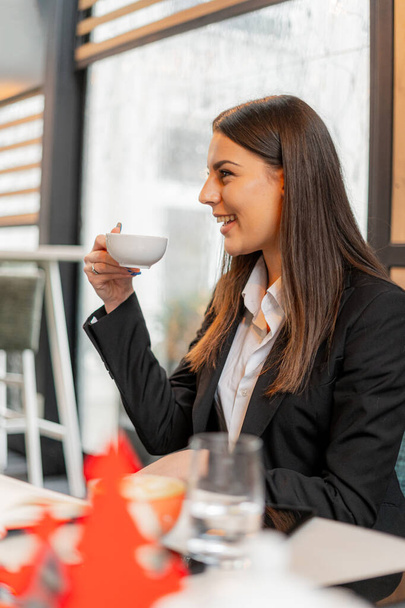 魅力的で美しい若い実業家がカフェで笑いながら彼女のお茶のカップを保持しています - 写真・画像