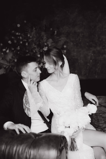 Das erste Treffen des Bräutigams im schwarzen Anzug und der Braut im weißen Brautkleid mit Blumenstrauß im Inneren eines Fotostudios, Hotels, auf schwarzem Hintergrund - Foto, Bild