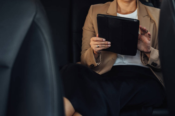 Onherkenbare vrouwelijke ondernemer Werken op Tablet Terwijl Zittend op de achterbank van een auto - Foto, afbeelding
