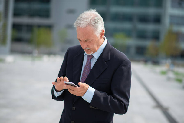 Portrait of a smiling senior businessman using his mobile smartphone outdoor - Foto, afbeelding