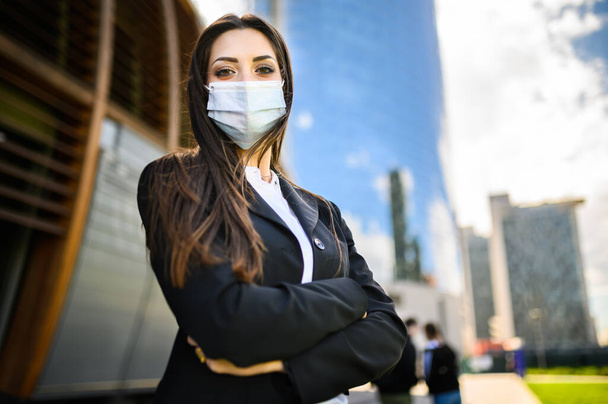 Fiduciosa giovane manager donna all'aperto in un ambiente urbano moderno e indossando una maschera protettiva contro la pandemia di covid 19 coronavirus - Foto, immagini