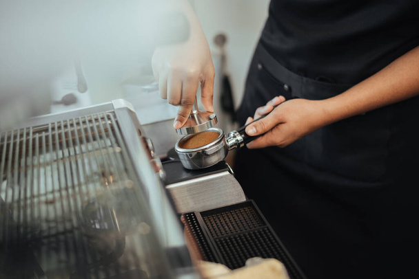 Barista verwendet einen Stampfer, um gemahlenen Kaffee in einen Portafilter zu pressen. Blick aus nächster Nähe auf Barista Hände Kaffee kochen mit Kaffeemaschine. Kaffeehaus-Konzept. - Foto, Bild