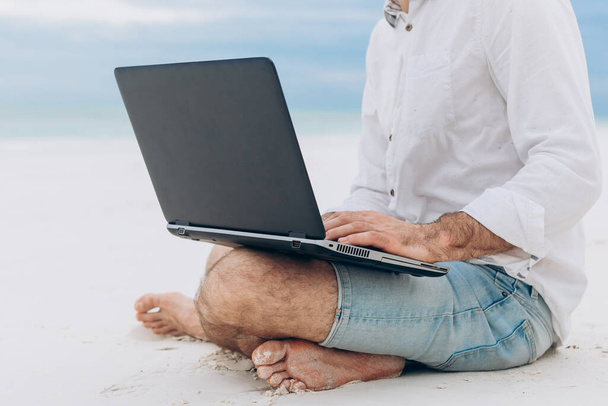 Un joven que usa un ordenador portátil en la playa. Relajación Vacaciones Trabajando al aire libre Beach Concept - Foto, Imagen