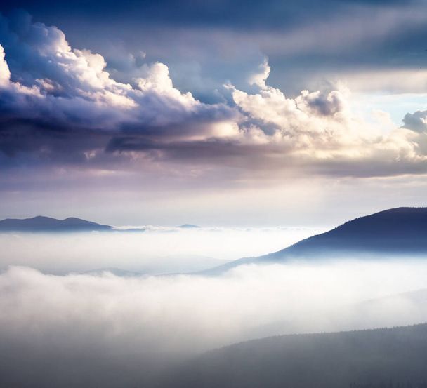 Nagyszerű kilátás a ködös hegyekre és a felhős égboltra, mely napfényben ragyog. Drámai és festői reggeli jelenet. Helyszín: Kárpátok, Ukrajna, Európa. Művészi kép. Szépségvilág.  - Fotó, kép