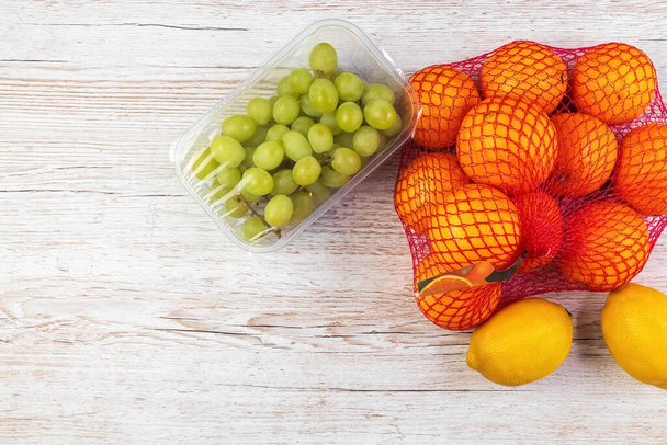 Świeże owoce na stole. Pomarańcze, cytryny, winogrona w opakowaniach detalicznych. Układy płaskie. - Zdjęcie, obraz