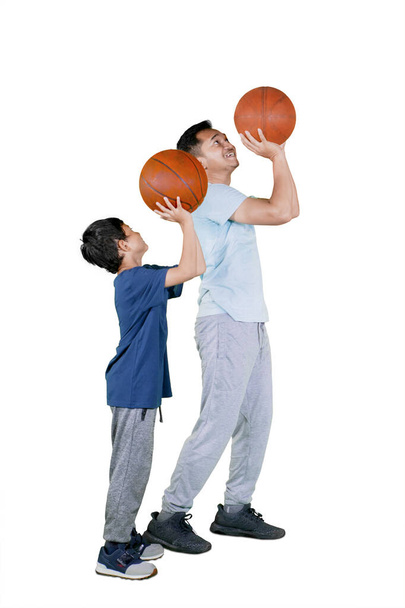 Happy father teaching his son to shooting a basketball while exercising together in the studio. Isolated on white background - Photo, Image