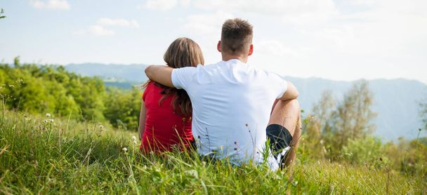 active couple rests on a mountain peak looking on a mountain landscape - Foto, imagen