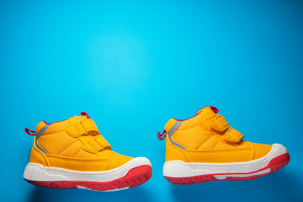 Κίτρινα παπούτσια μωρού. Παιδικά αθλητικά παπούτσια απομονωμένα σε μπλε φόντο - Φωτογραφία, εικόνα