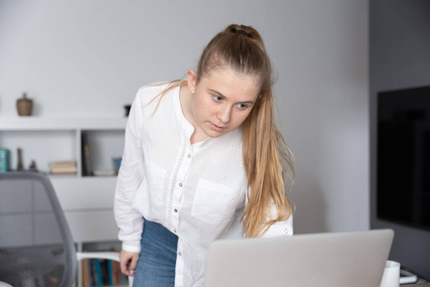 Νεαρή ελεύθερη επαγγελματίας στέκεται ενώ ελέγχει το laptop της. Εργασία από το σπίτι έννοια - Φωτογραφία, εικόνα