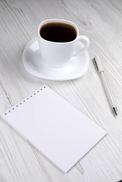 Біла чашка кави, блокнот і біла ручка на дерев'яному столі, вид зверху
 - Фото, зображення
