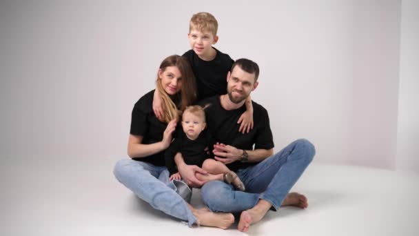 Onnellinen perhe istuu poseeraa yhdessä äiti ja isä, poika poika ja lapsi pieni tytär nauttia yhdessä - Materiaali, video