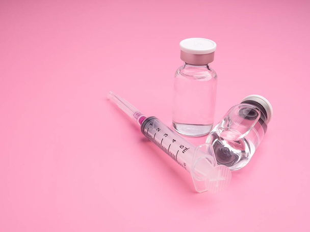Il vaccino in flaconi di vetro con una siringa posta su uno sfondo rosa chiaro. Vaccino per l'immunizzazione e trattamento dall'infezione da virus. Vista dall'alto. Concetto di auto medica e sanitaria. - Foto, immagini