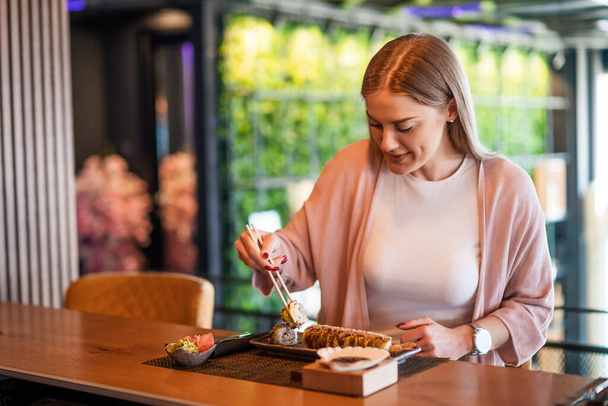 Szczęśliwa kobieta je sushi z pałeczkami w restauracji sushi. - Zdjęcie, obraz