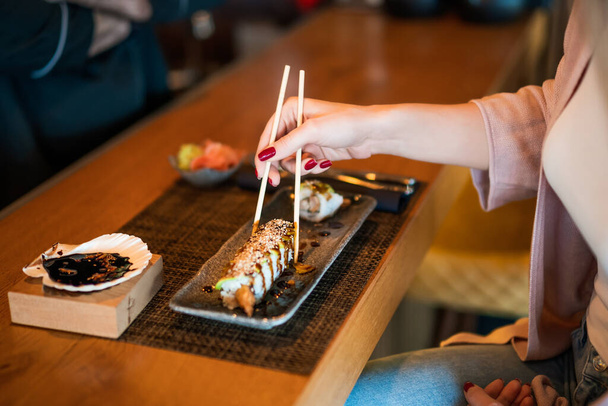 寿司屋で箸で旨味寿司を食べている女性のクローズアップ. - 写真・画像