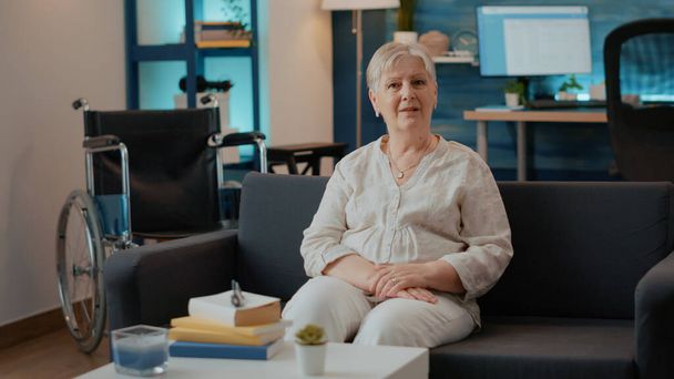 Portrait of retired woman with disability sitting on sofa - Valokuva, kuva