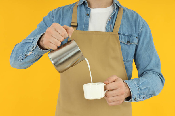 Waiter or barista pour milk on yellow background - Foto, Imagen