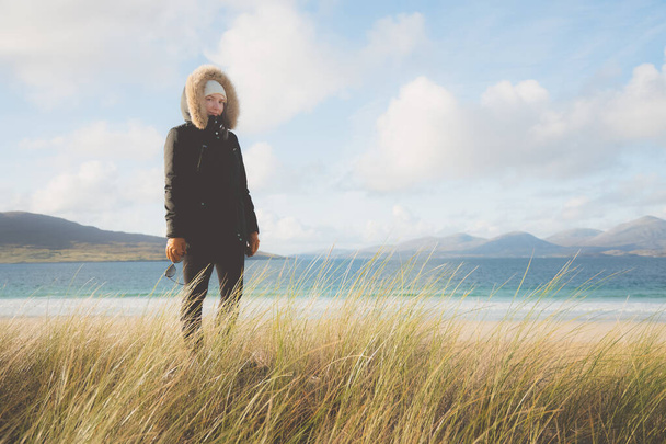 Eine junge Touristin im Wintermantel besucht den weißen Sandstrand und die grasbewachsenen Dünen von Luskentyre Beach auf der Isle of Lewis und Harris in den Äußeren Hebriden Schottlands. - Foto, Bild