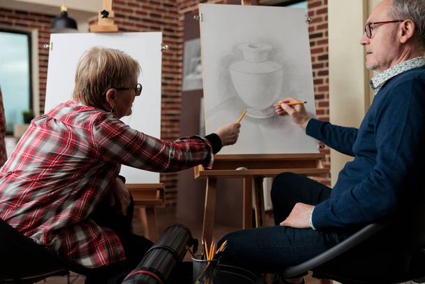 Professora idosa explicando aula de ilustração ao aluno durante curso de arte - Foto, Imagem