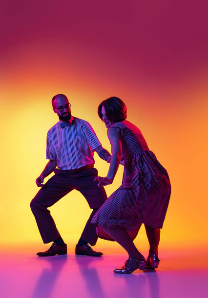 Retrato de hombre y mujer excitados, pareja de bailarines en trajes de estilo retro vintage bailando lindy hop danza aislada sobre fondo amarillo degradado y púrpura. - Foto, Imagen