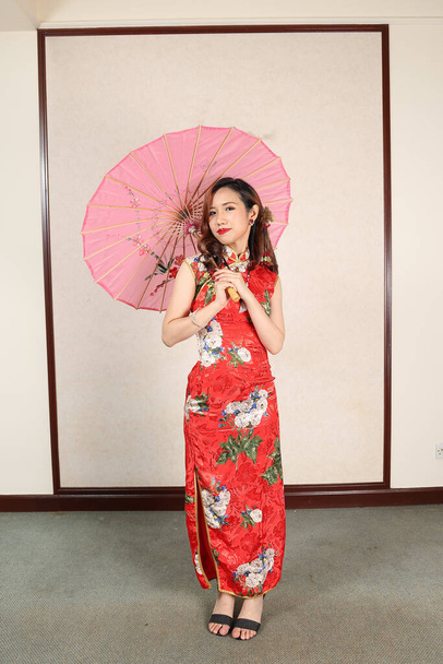 Çekici genç bir kadın eski Çin Cheongsam elbisesi giyiyor renkli kağıt şemsiye pozu veriyor. - Fotoğraf, Görsel