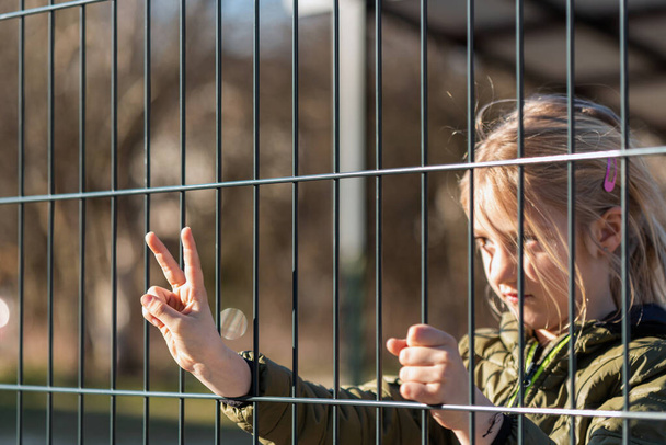 Child refugee behind a metal fence - Фото, изображение